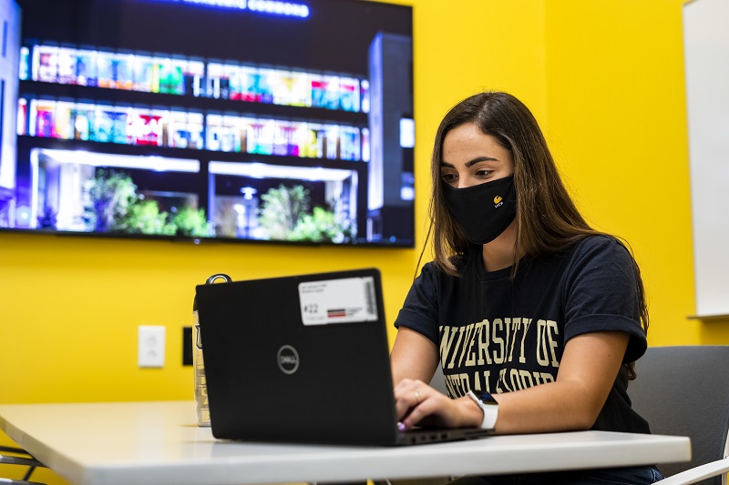 A UCF student sits at a desk in front of a computer.