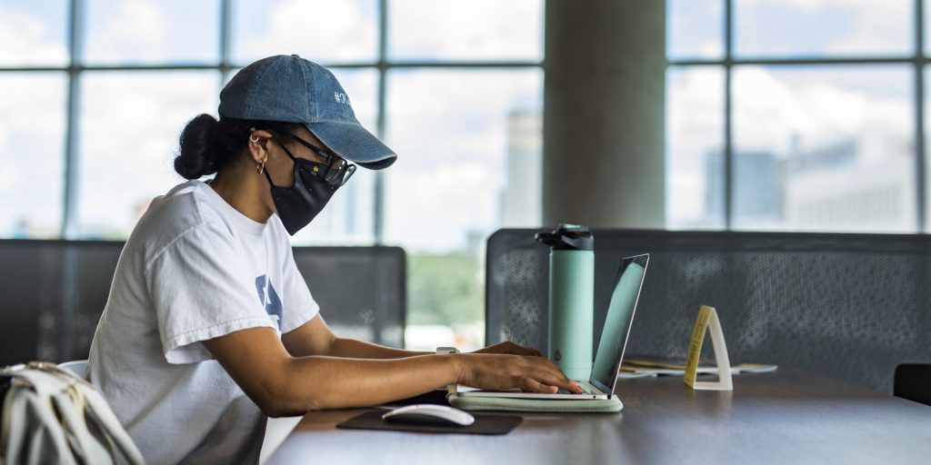 Student wearing a mask in front of computer inside.
