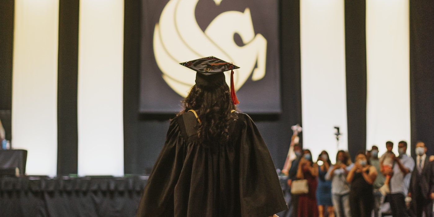 Student walks in cap and gown towards large Pegasus